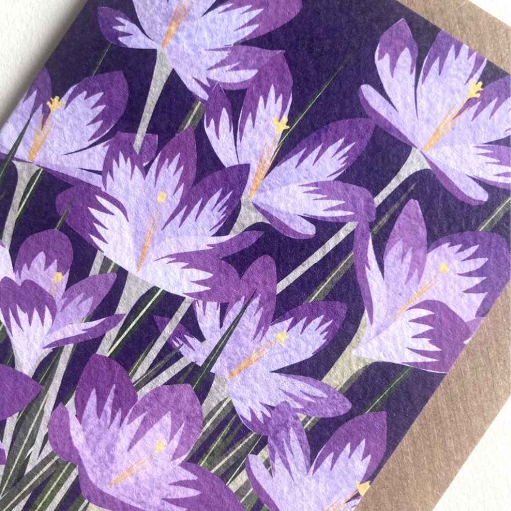 A close-up of a purple and lavender floral pattern, likely a greeting card or printed paper item, featuring stylized crocuses on a dark purple background with a brown kraft paper edge visible at the right.