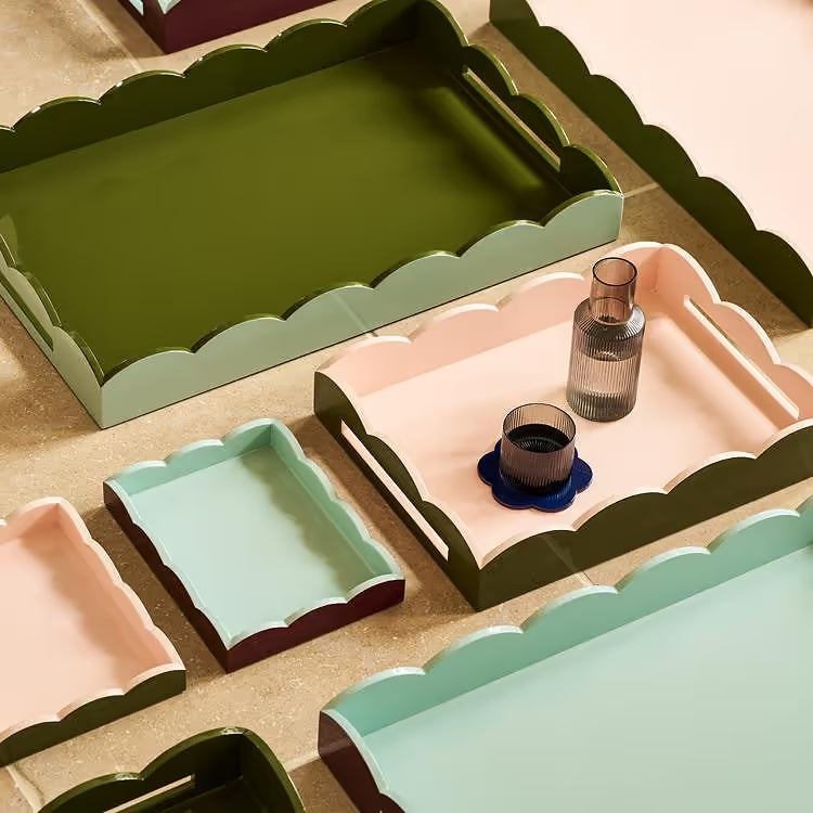 Set of decorative trays with scalloped edges in various colors on a beige surface.